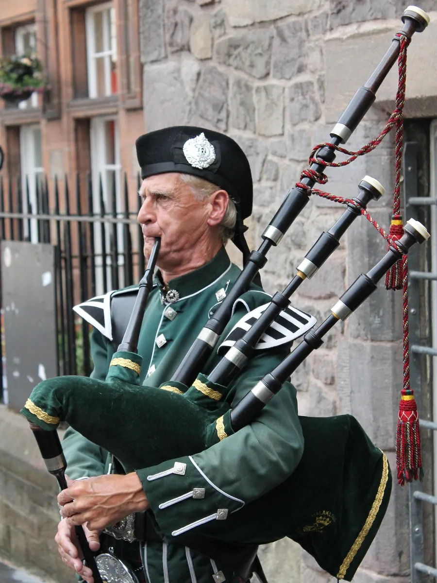 A person dressed in traditional Scottish attire playing a set of bagpipes A person dressed in traditional Scottish attire playing a set of bagpipes